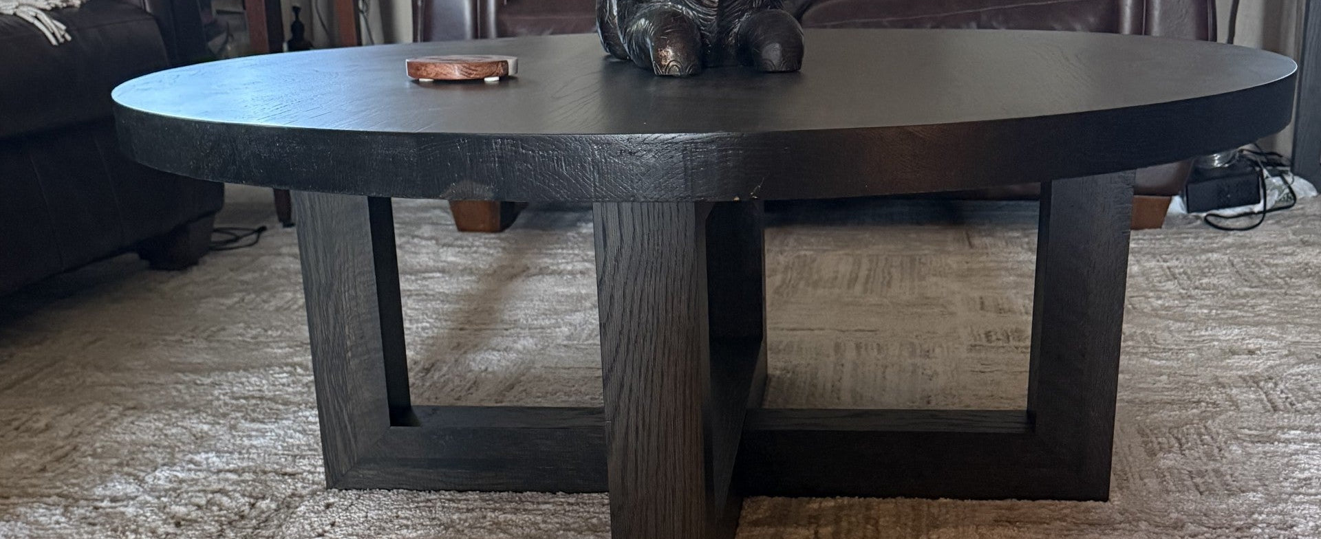 A dark round coffee table with a thick rectangular base, shown in a living room setting on a textured carpet.